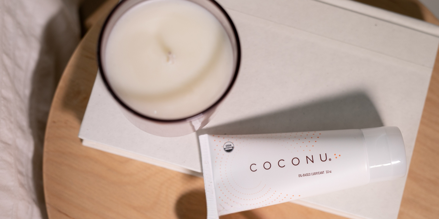Coconu oil-based lubricant beside a candle and towels, representing an organic coconut massage oil for couples