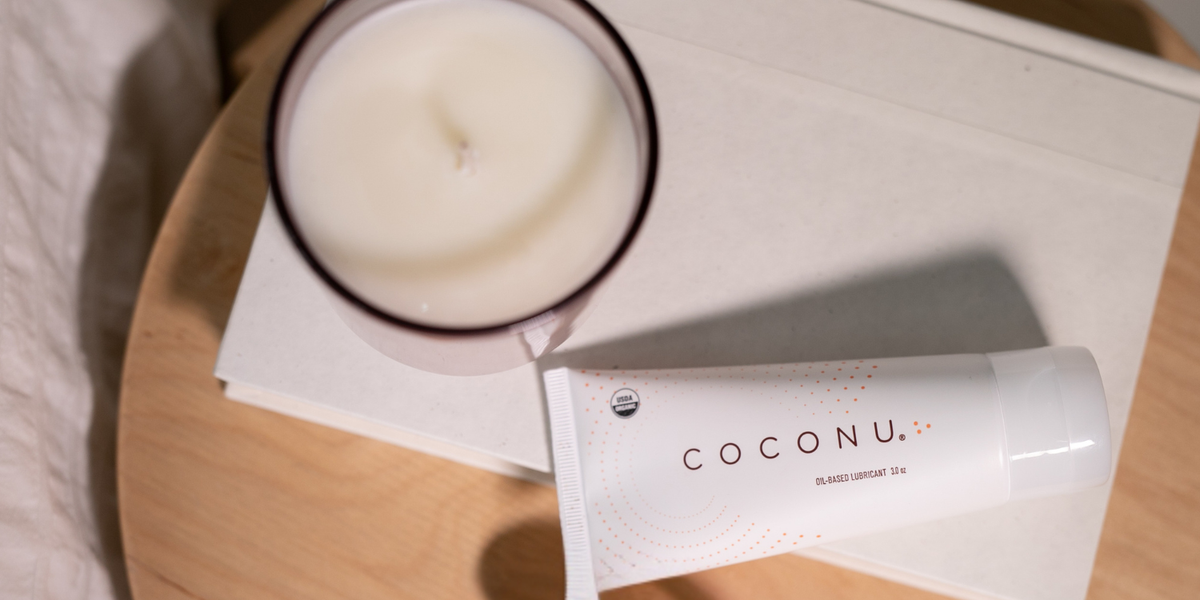 Coconu oil-based lubricant beside a candle and towels, representing an organic coconut massage oil for couples
