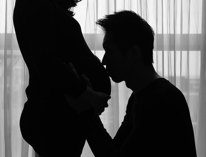 Intimate black-and-white silhouette of a husband kissing his pregnant wife's stomach