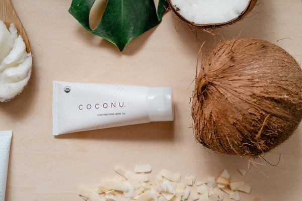 Coconu oil-based lubricant on a clean surface beside natural ingredients, representing edible, food-safe intimate care