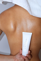 Person with a towel wrapped on their head holding a Coconu body oil tube