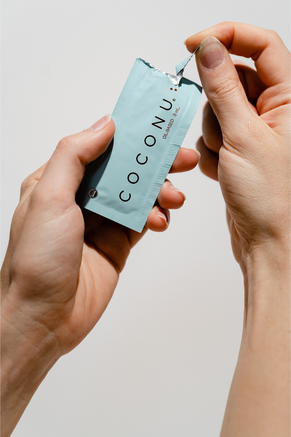 Hands tearing open a light blue Coconu single-use lubricant sachet