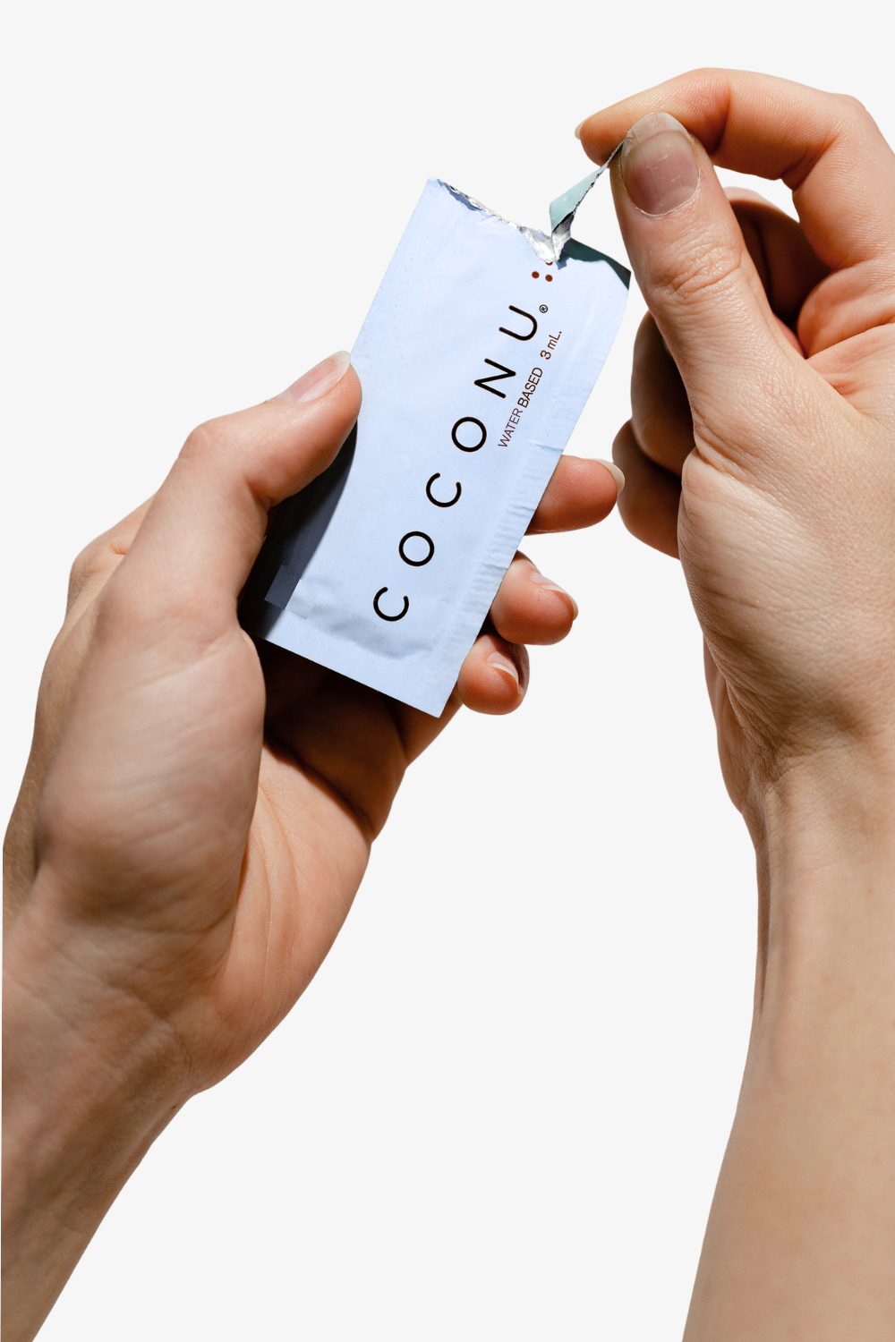Hands tearing open a white Coconu single-use lubricant sachet