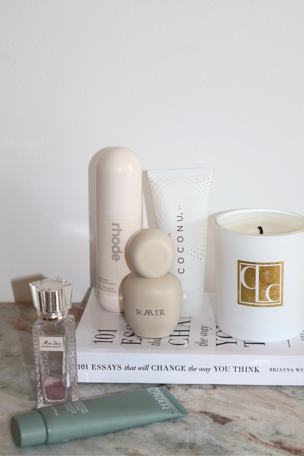 Coconu body oil tube on a shelf with a candle, diffuser and skincare bottles
