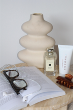 Coconu tubes on a bedside table with a vase, perfume, glasses and an open book