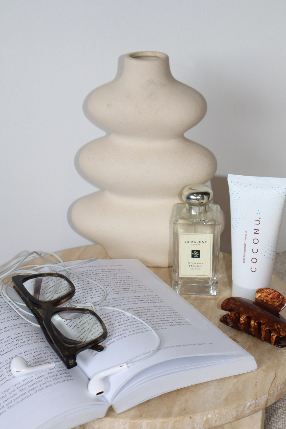 Coconu tubes on a bedside table with a vase, perfume, glasses and an open book