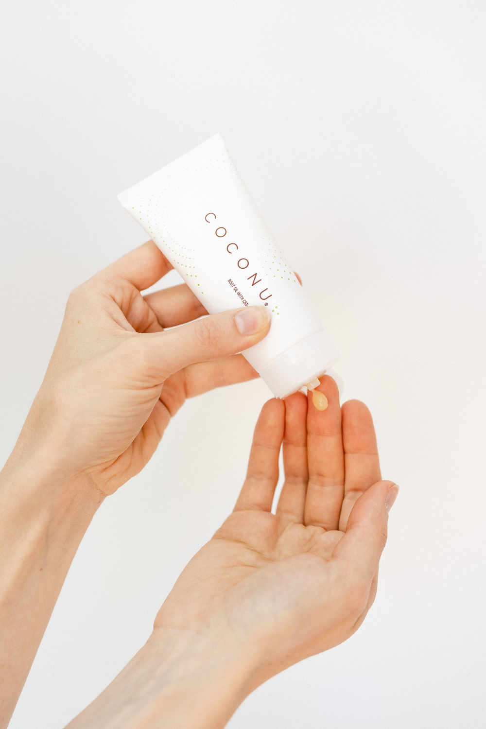 Hands easing Coconu hemp-infused body oil from the tube into an open palm