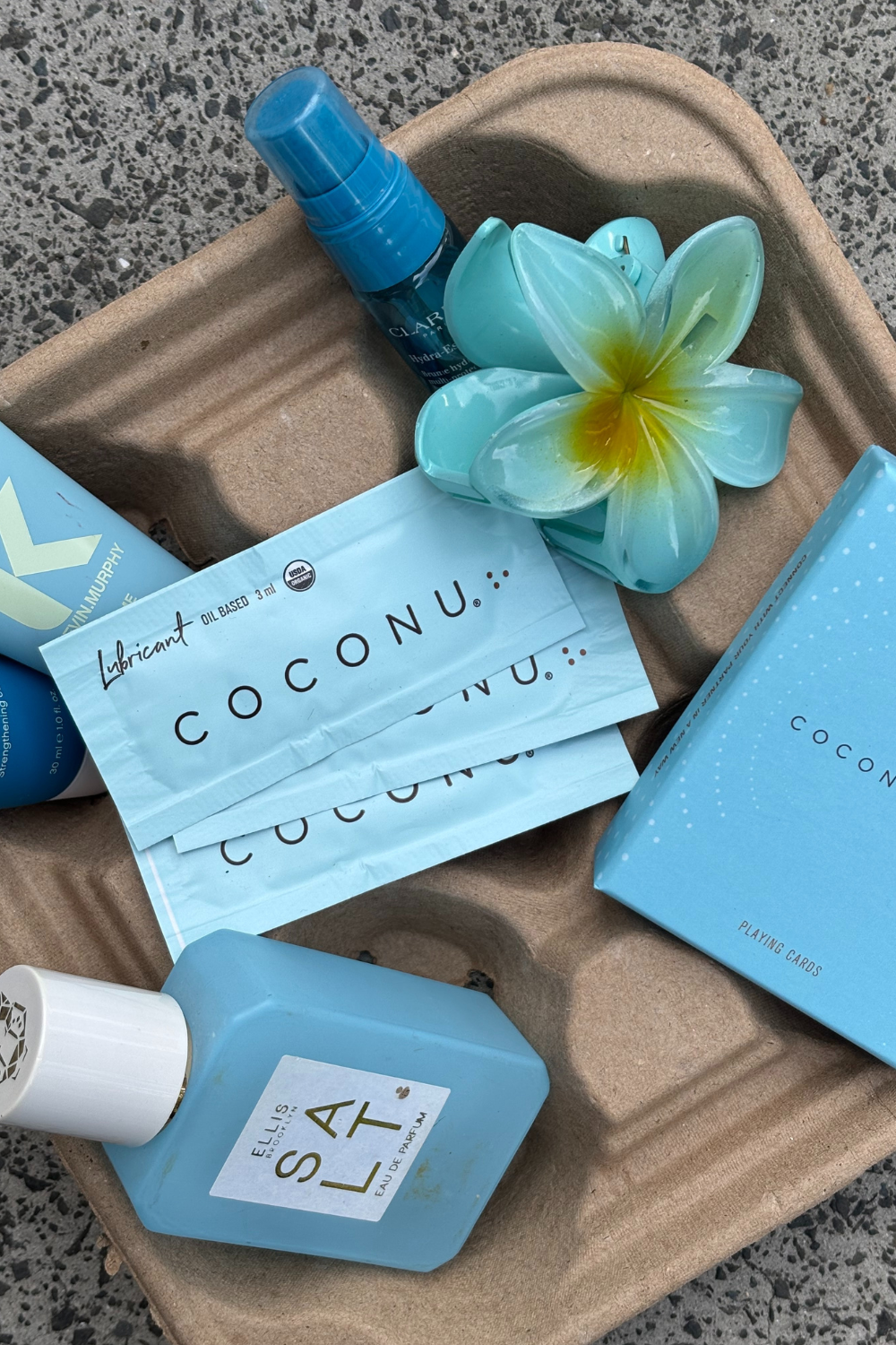 Coconu sachets and carton on a moulded tray with a blue bottle and frangipani flower