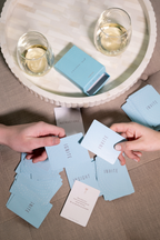 Two people drawing Coconu Connect cards from a scattered pile beside glasses of wine