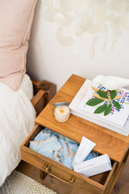 Coconu tubes and a candle in an open bedside drawer beside a made bed