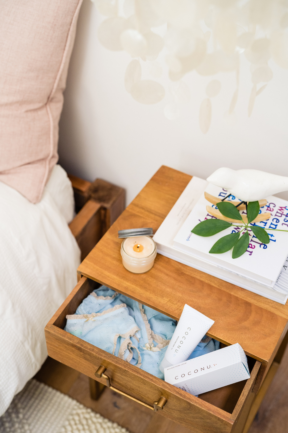 Coconu tubes and a candle in an open bedside drawer beside a made bed