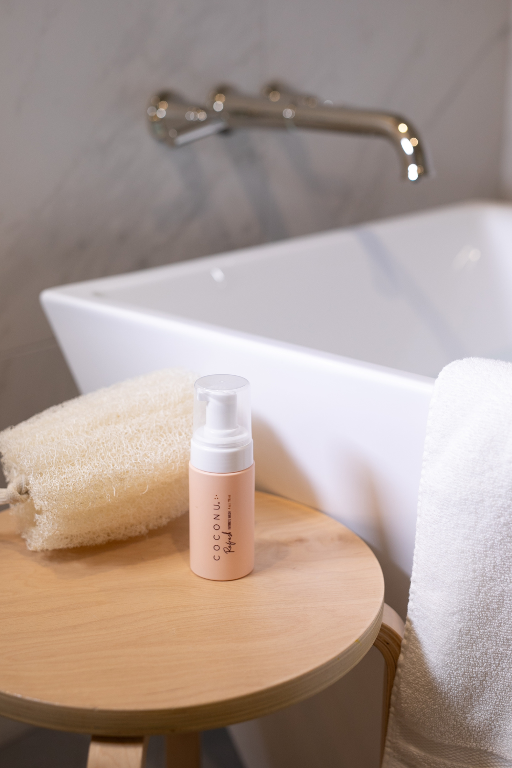 Coconu Refresh intimate wash on a wooden stool beside a bathtub and folded towels