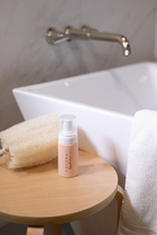 Coconu Refresh intimate wash on a wooden stool beside a bathtub and folded towels
